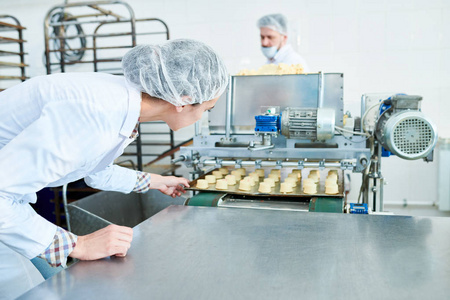 糖果厂雇员在头发网举行烘烤板材与未加工的糕点, 当操作机器时